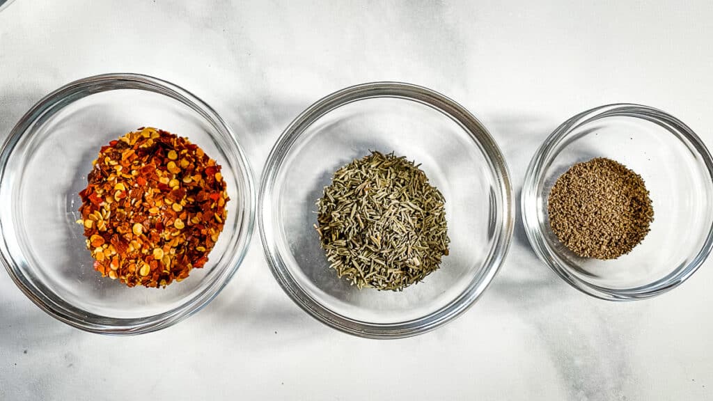Bowls of seasonings. From left to right: red pepper flakes, dried thyme, and ground black pepper.