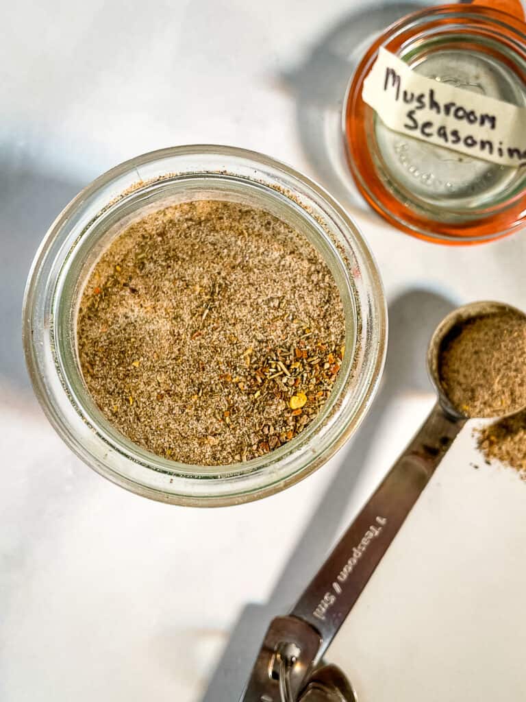 Homemade mushroom seasoning in jar. Teaspoon and lid sit off to the right side.