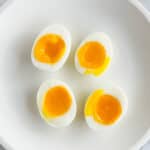 Soft boiled eggs on a white plate. Cut in half to show runny, yellow yolk.