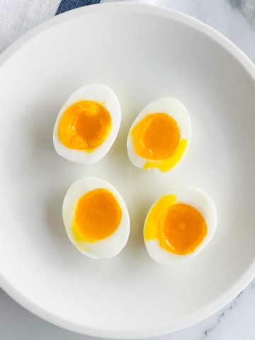 Soft boiled eggs on a white plate. Cut in half to show runny, yellow yolk.