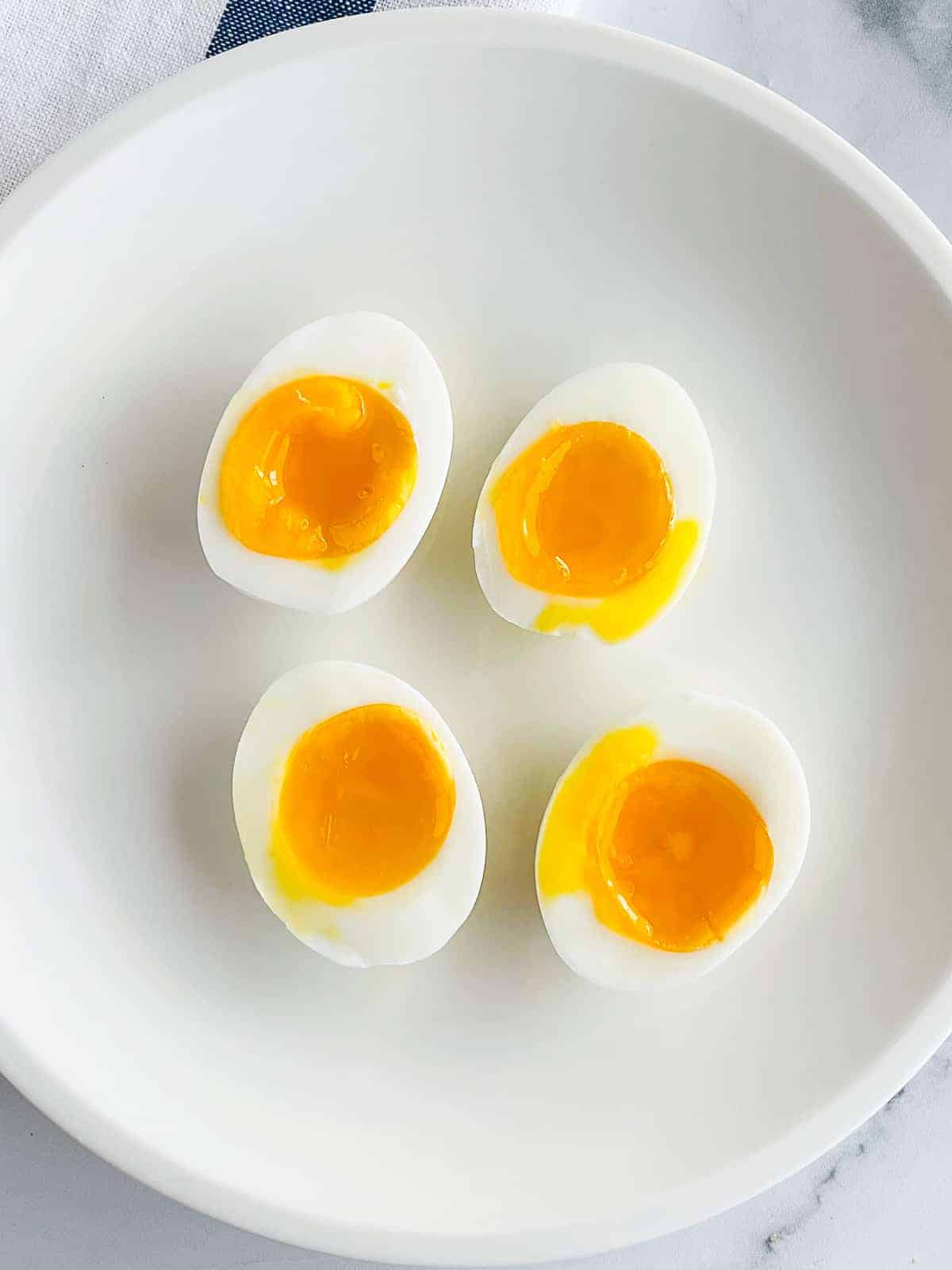 Two soft-boiled eggs, cut in half, on a white plate. Yolks are runny and soft.