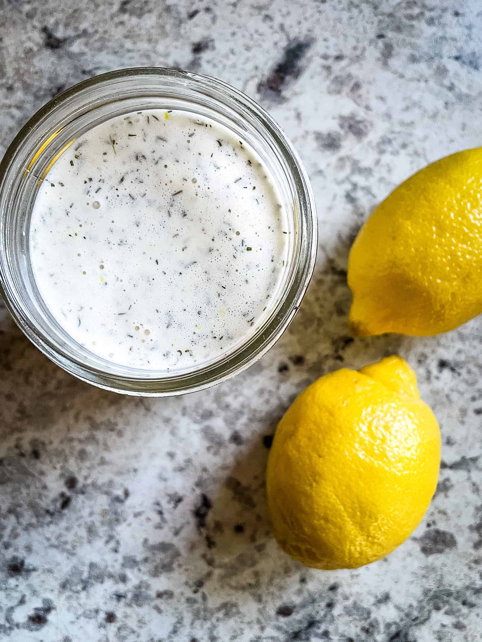 Creamy lemon pepper dressing in a jar. Two lemons are on the side.