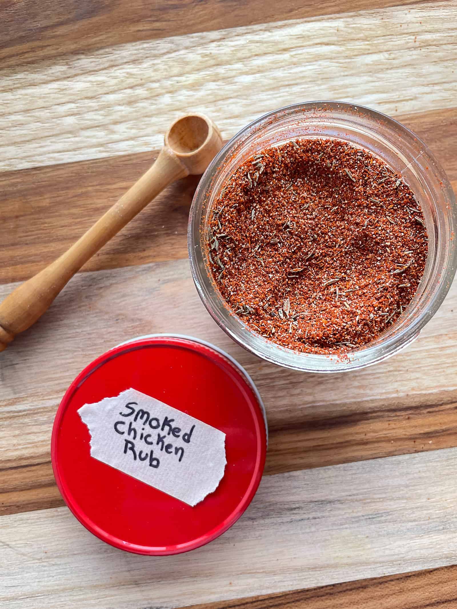 Smoked chicken rub in a small jar. Lid and scoop placed to the left of jar.