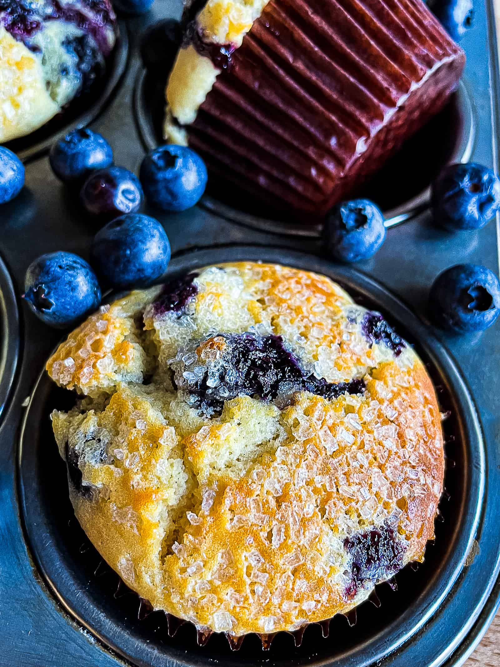 Baked blueberry muffin in a pan. Fresh blueberries are scattered on the pan.