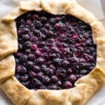 Baked blueberry galette on a serving plate. A piece of parchment paper is under the galette.