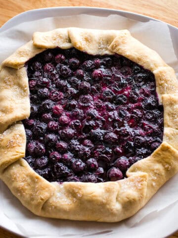 Baked blueberry galette on a serving plate. A piece of parchment paper is under the galette.