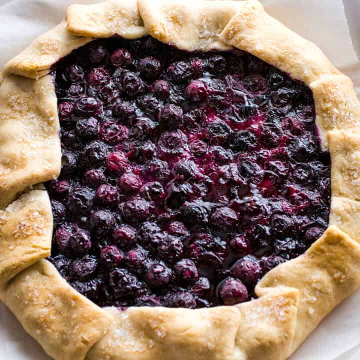 Baked blueberry galette on a serving plate. A piece of parchment paper is under the galette.
