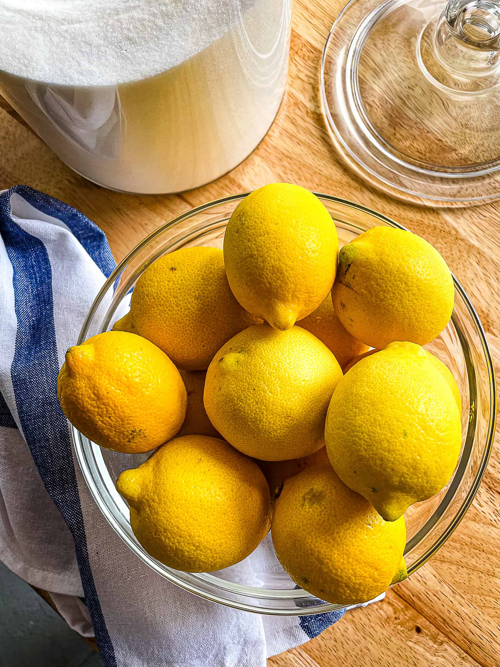 Bowl of lemons with a jar of sugar in the background.
