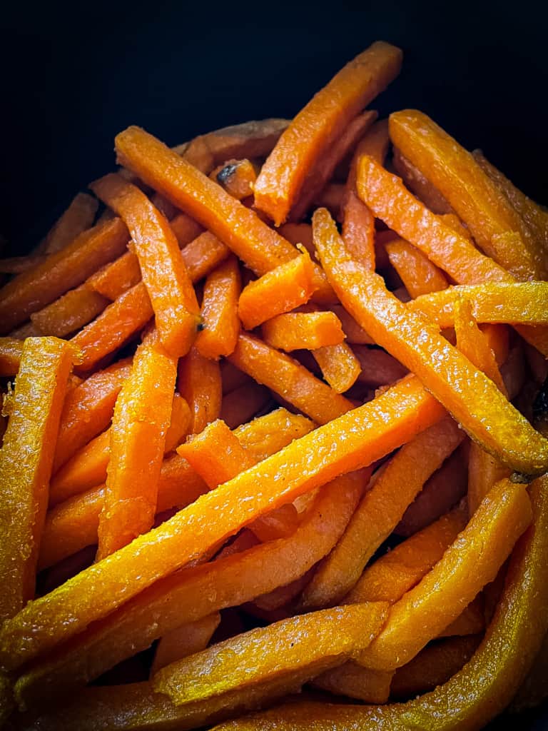 Frozen sweet potatoes after being cooked for three minutes in an air fryer. There is a slight glisten on the fries.