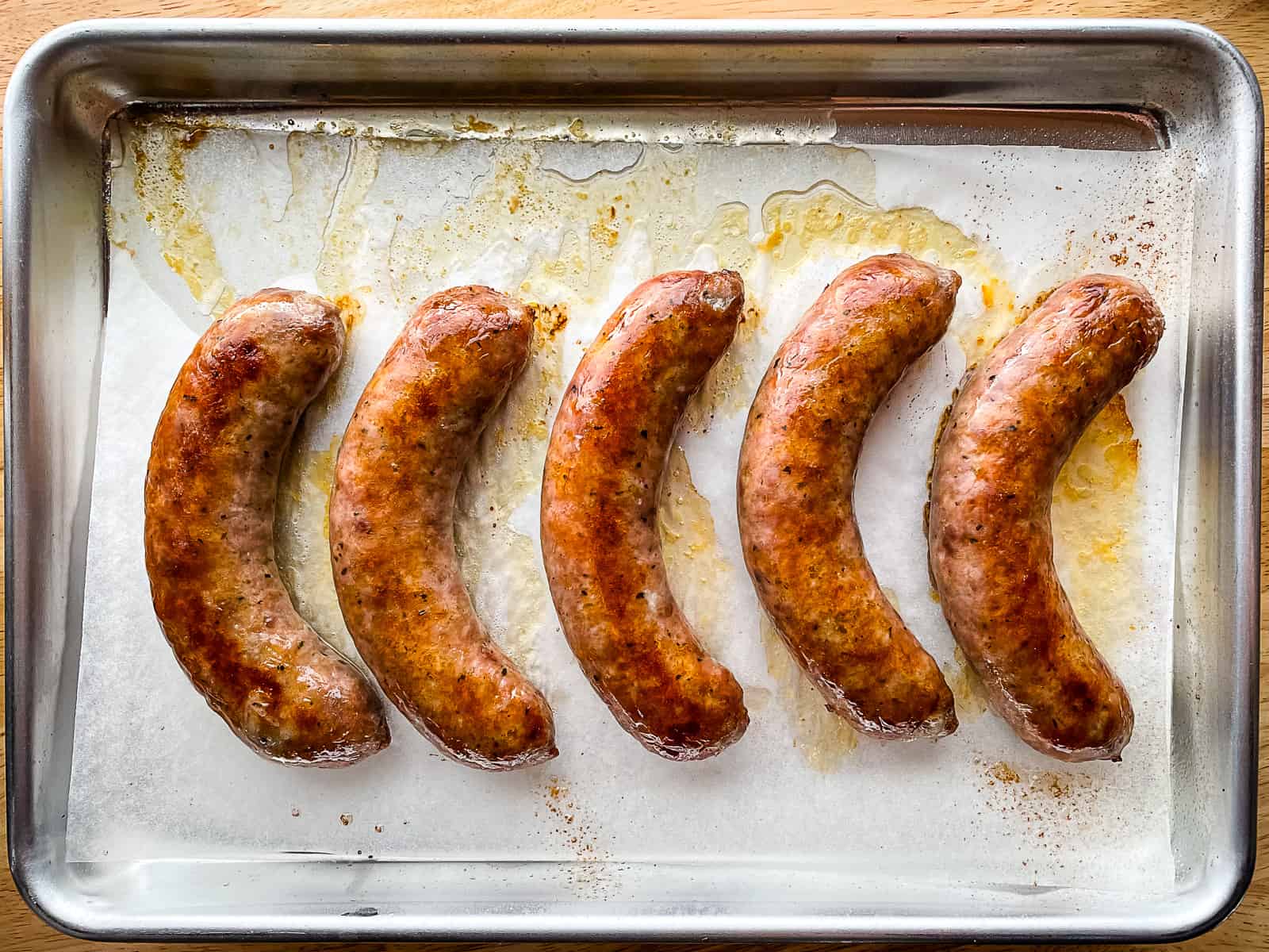 Five oven cooked sausage on a baking sheet.