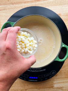 Adding white chocolate chips to a pot of white chocolate sauce.