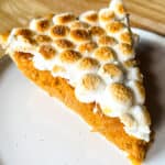 Slice of sweet potato casserole pie on a plate. The filling is orange and the slice is topped with browned marshmallows.