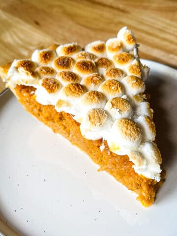 Slice of sweet potato casserole pie on a plate. The filling is orange and the slice is topped with browned marshmallows.