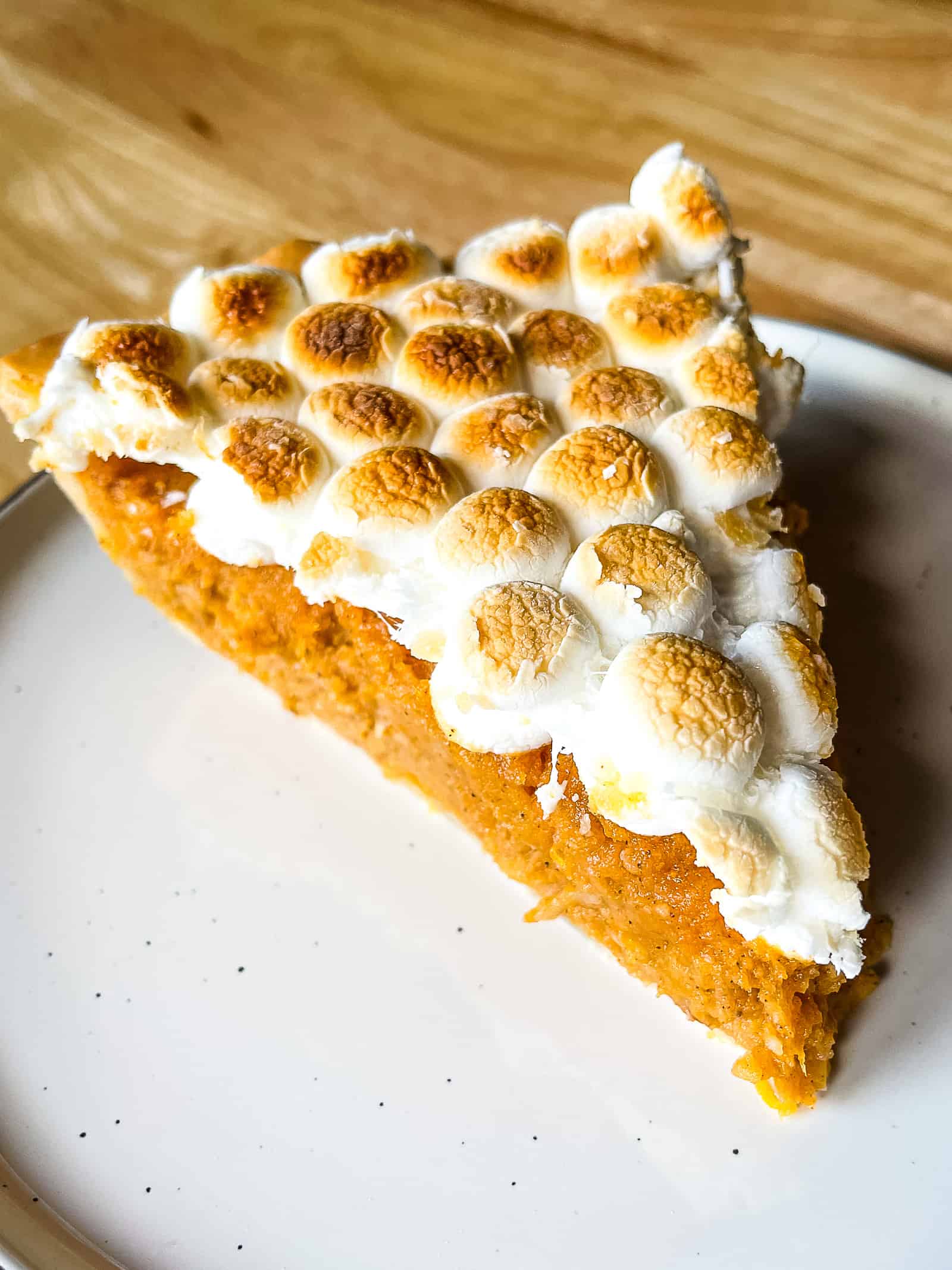 Slice of sweet potato casserole pie on a plate. The filling is bright orange and is topped with browned mini marshmallows.