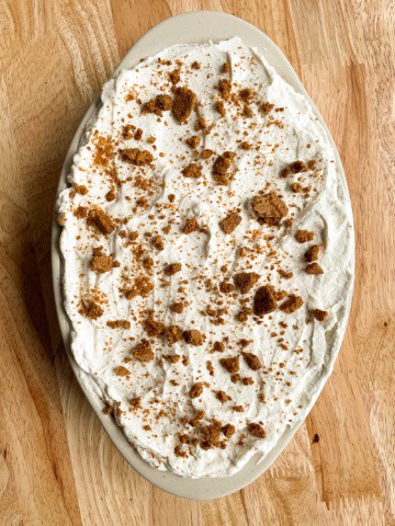 Gingersnap icebox cake in an oval baking dish. Gingersnap crumbs are sprinkled on top of the maple whipped cream.