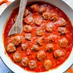 Pan of baked meatballs in pasta sauce. A wooden spoon sits off to the side.