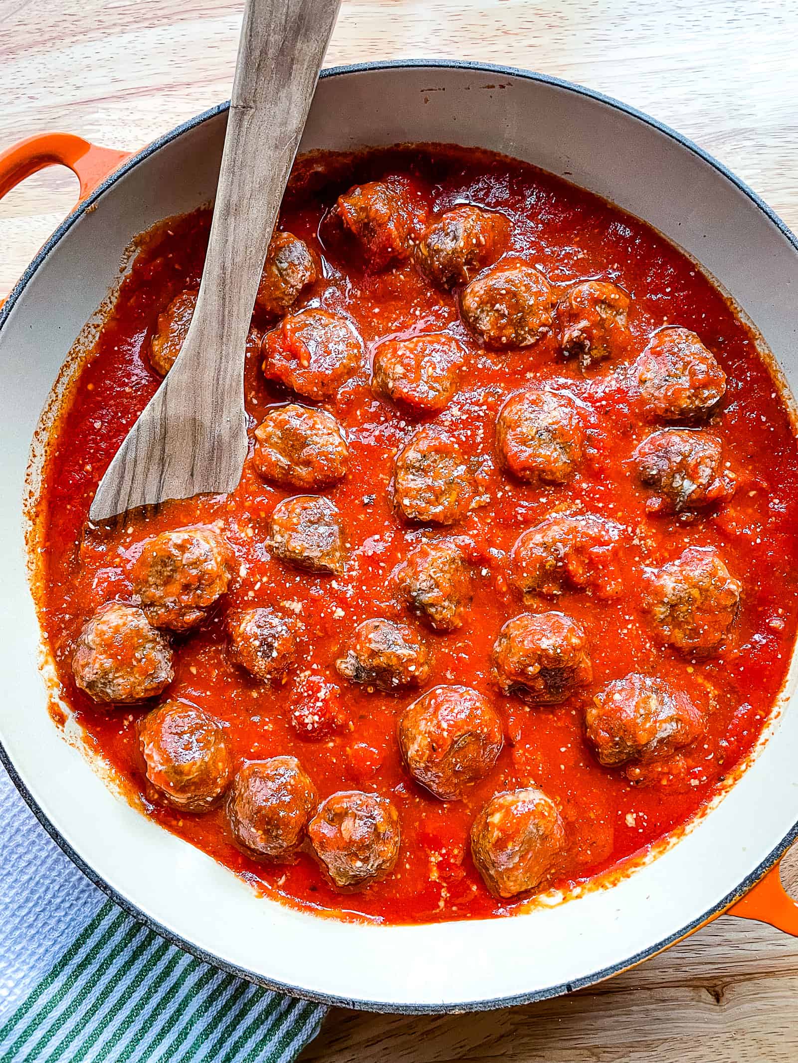 Pan of baked meatballs in pasta sauce. A wooden spoon sits off to the side.