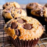 Brown butter chocolate chip muffins cooling on a wire rack. The muffins are in brown muffin liners. A few chocolate chips are on top of the muffins.