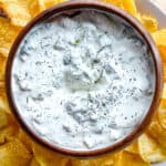 Dill pickle dip in a bowl surrounded by potato chips.