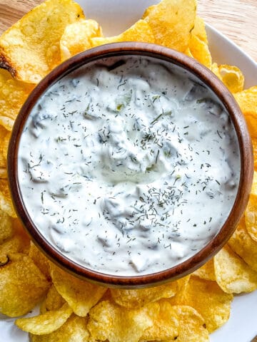 Dill pickle dip in a bowl surrounded by potato chips.