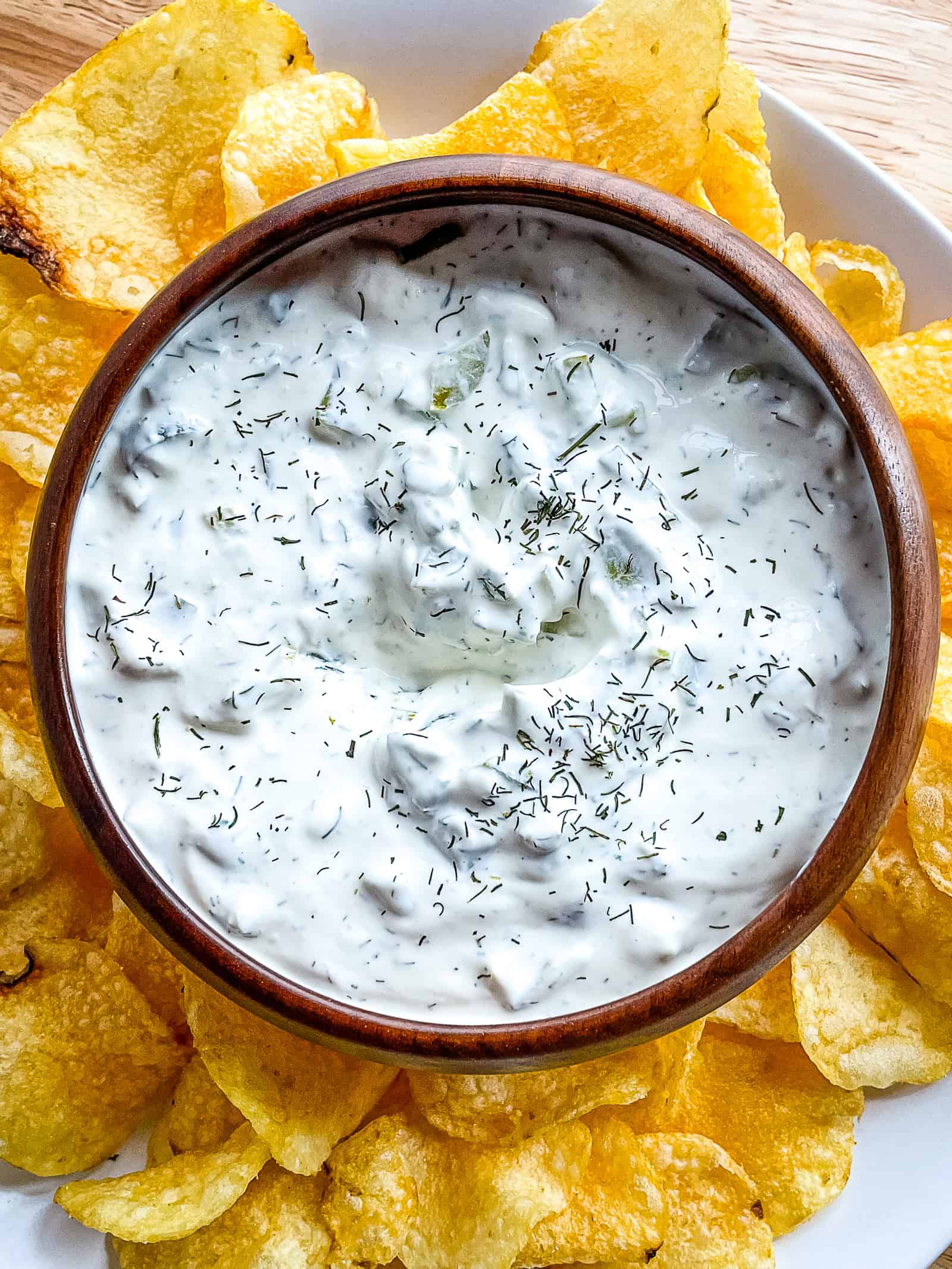 Dill pickle dip in a bowl surrounded by potato chips. 