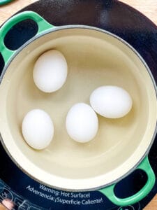 Four hard boiled eggs in a small green pot.