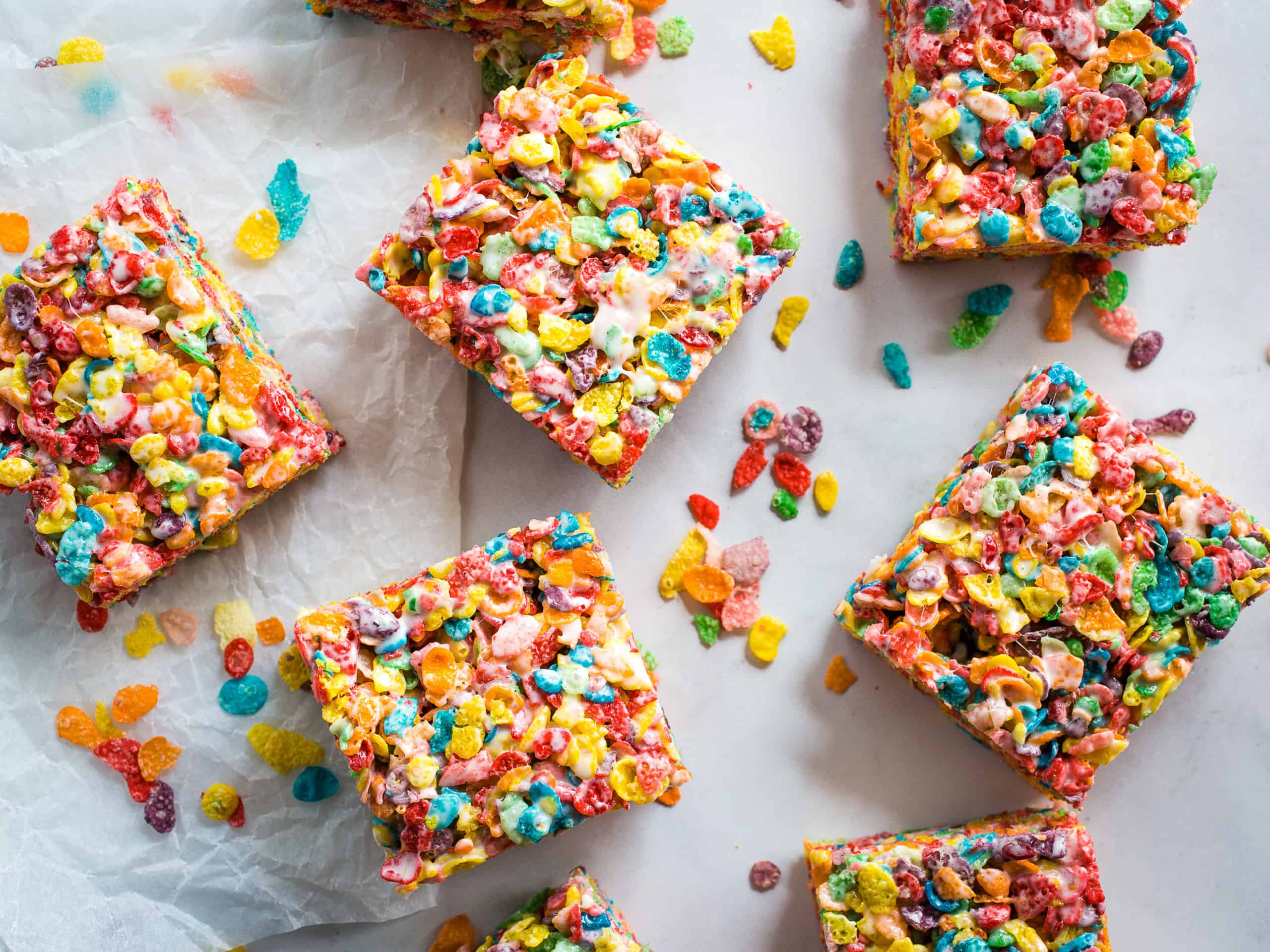 Fruity Pebbles bars cut on a table with Fruity Pebbles cereal sprinkled around. 