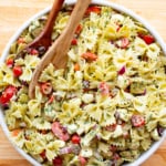 Bowl of basil pasta salad in a white bowl. Two wooden spoons are set in the left of the bowl.