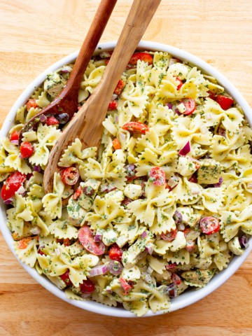 Bowl of basil pasta salad in a white bowl. Two wooden spoons are set in the left of the bowl.