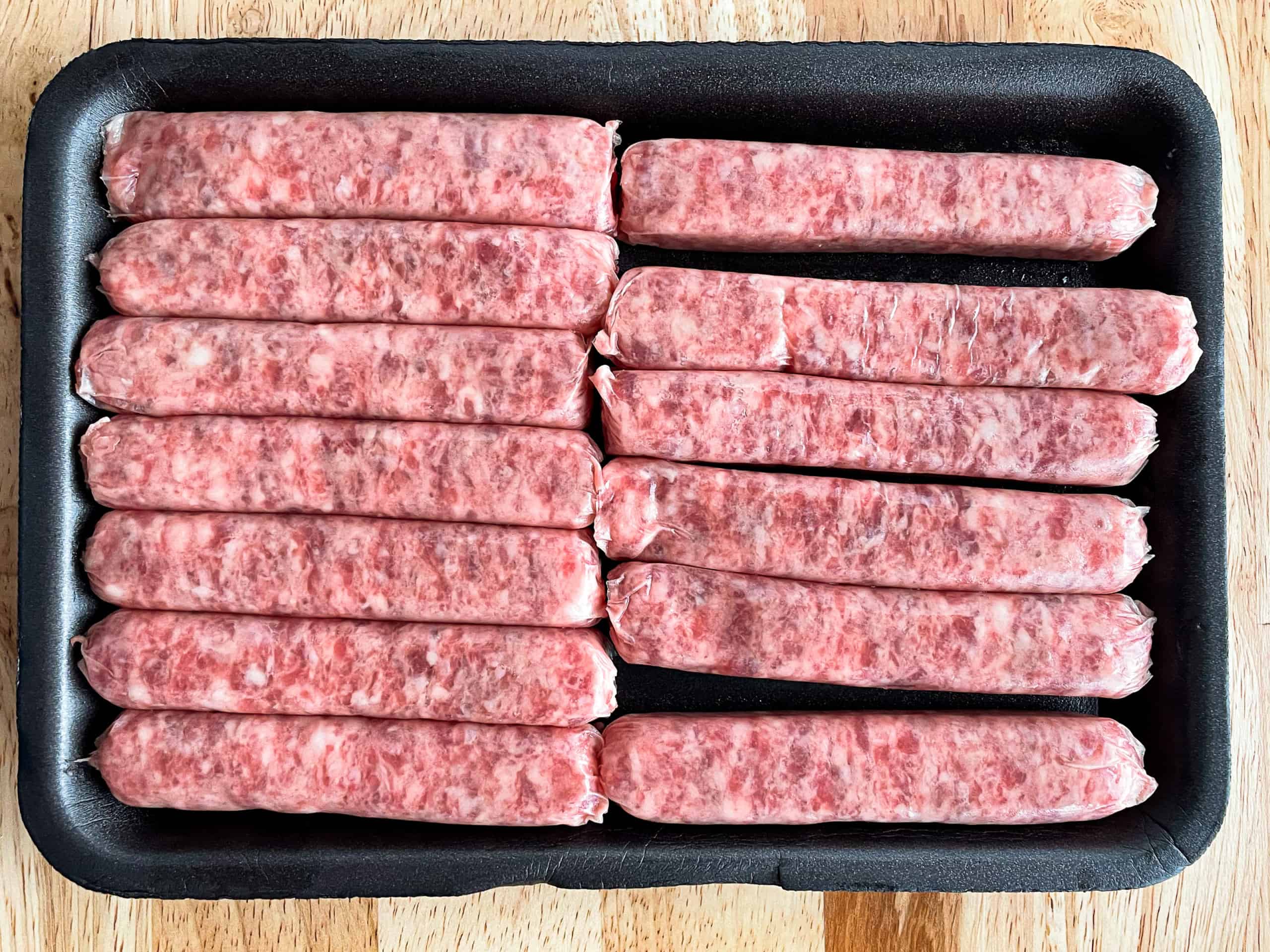 Fresh, uncooked breakfast sausage links on a black tray.