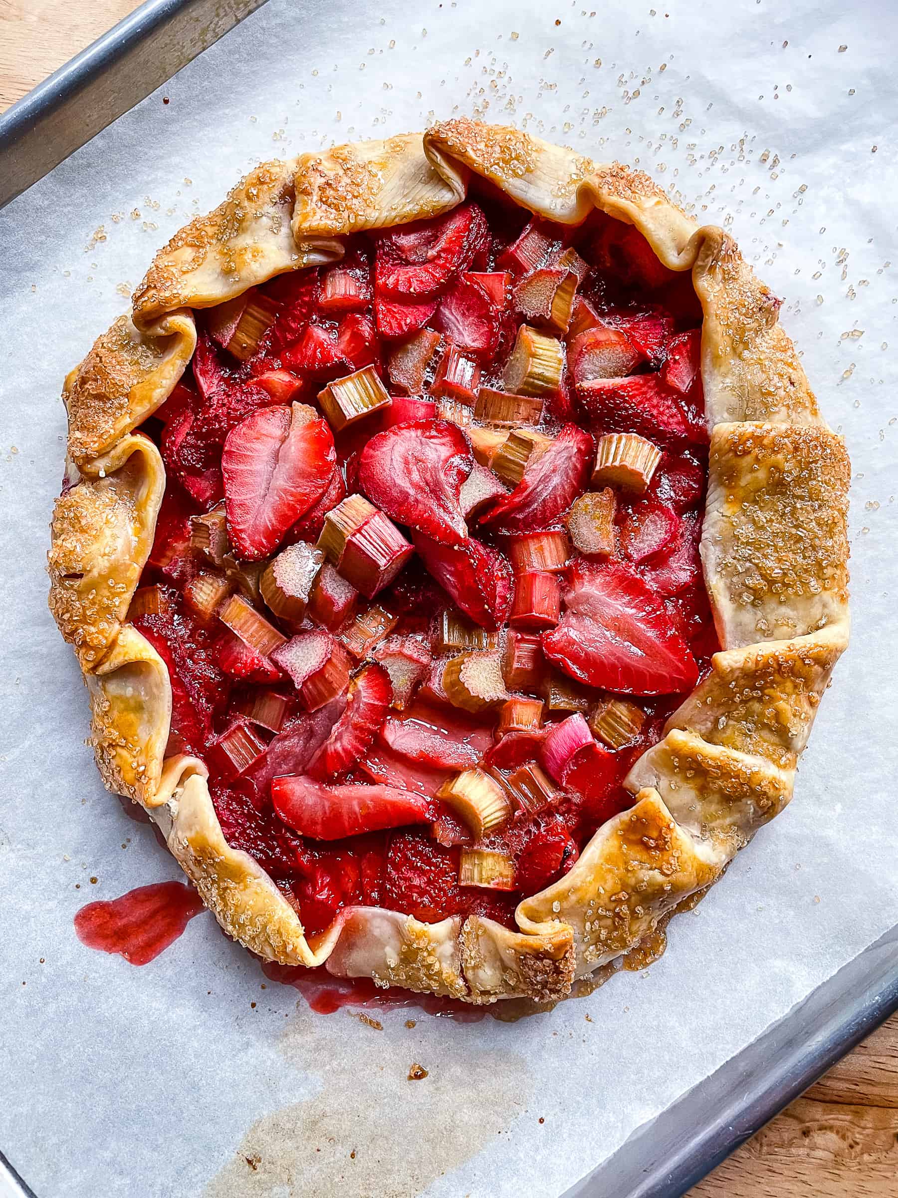 A strawberry-rhubarb galette cooling on a parchment-lined sheet pan.