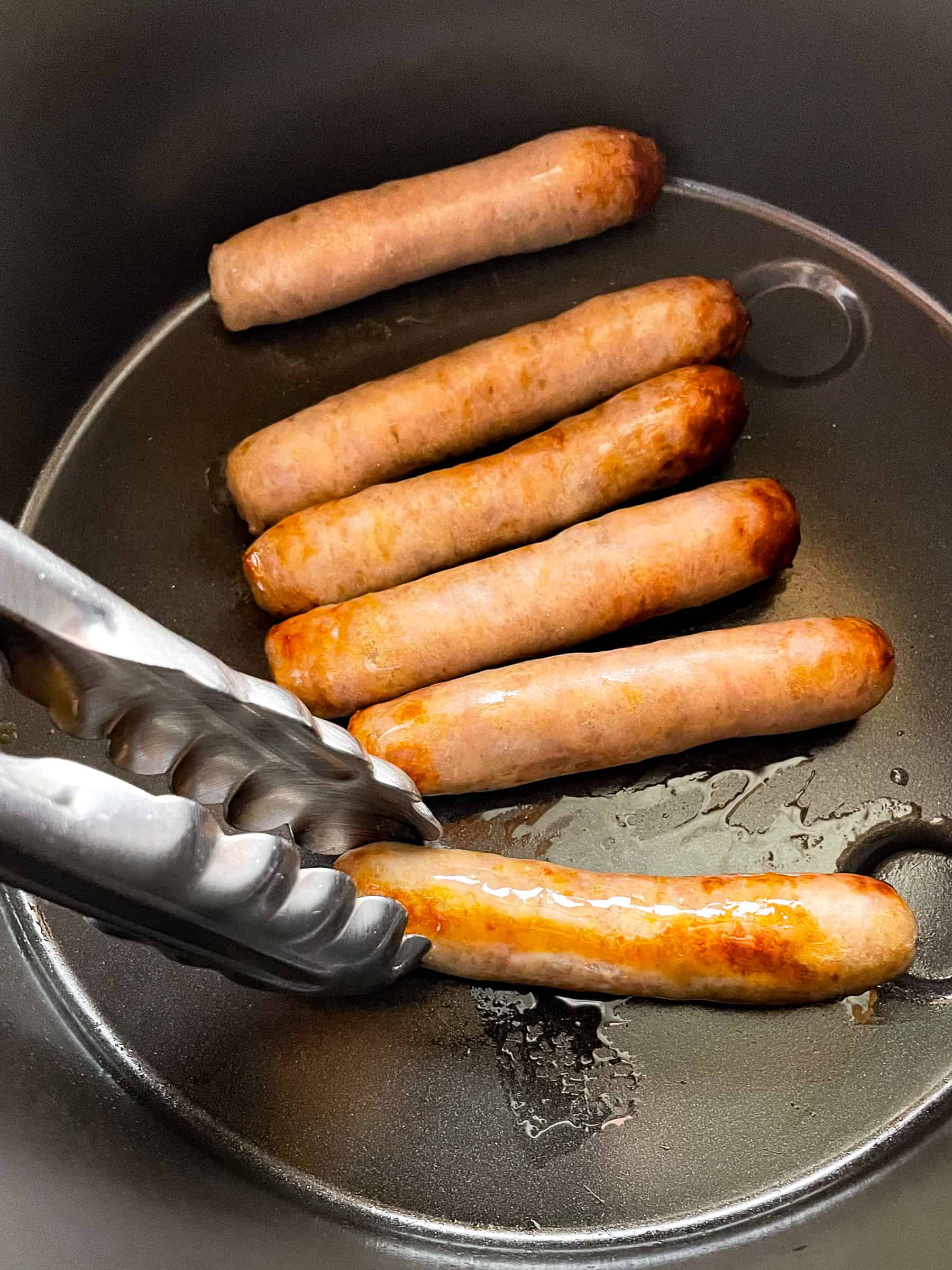 Turning breakfast sausage links in the air fryer with a pair of tongs.