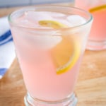 Glass of pink lemonade with ice cubes and a lemonade wedge.