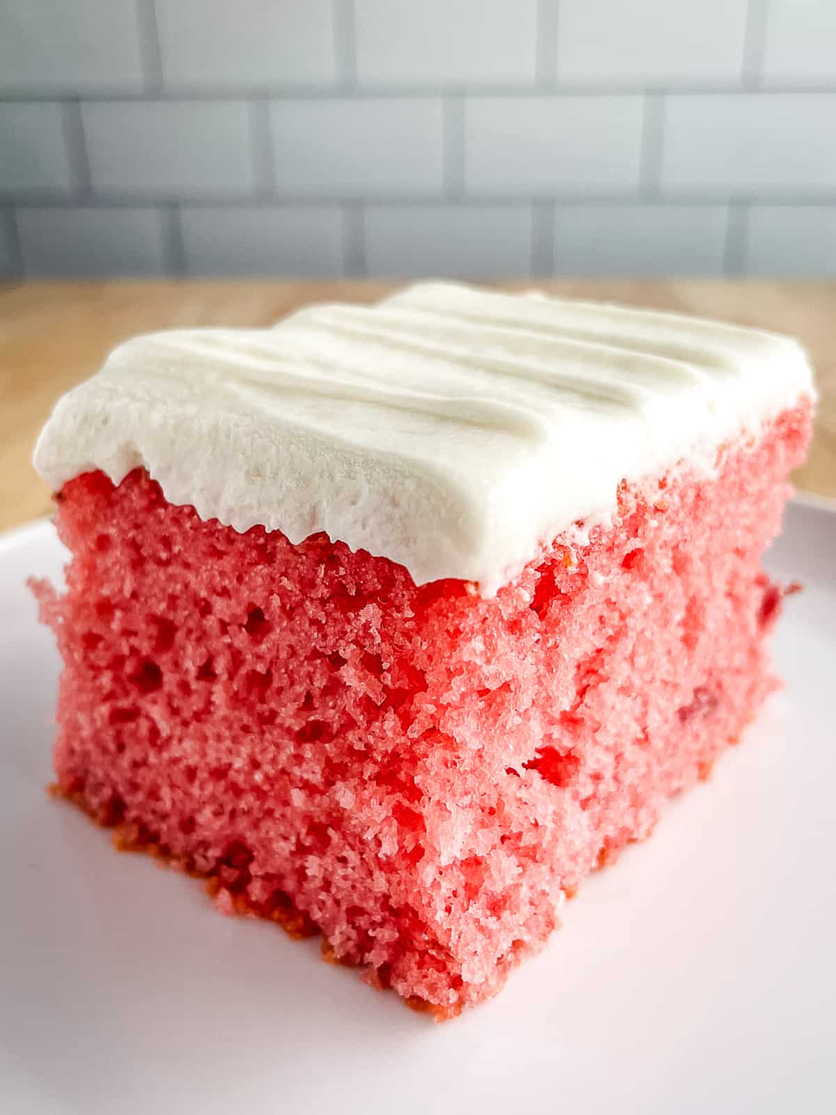 Slice of strawberry cake on a plate. Cake is frosted with cream cheese frosting. 