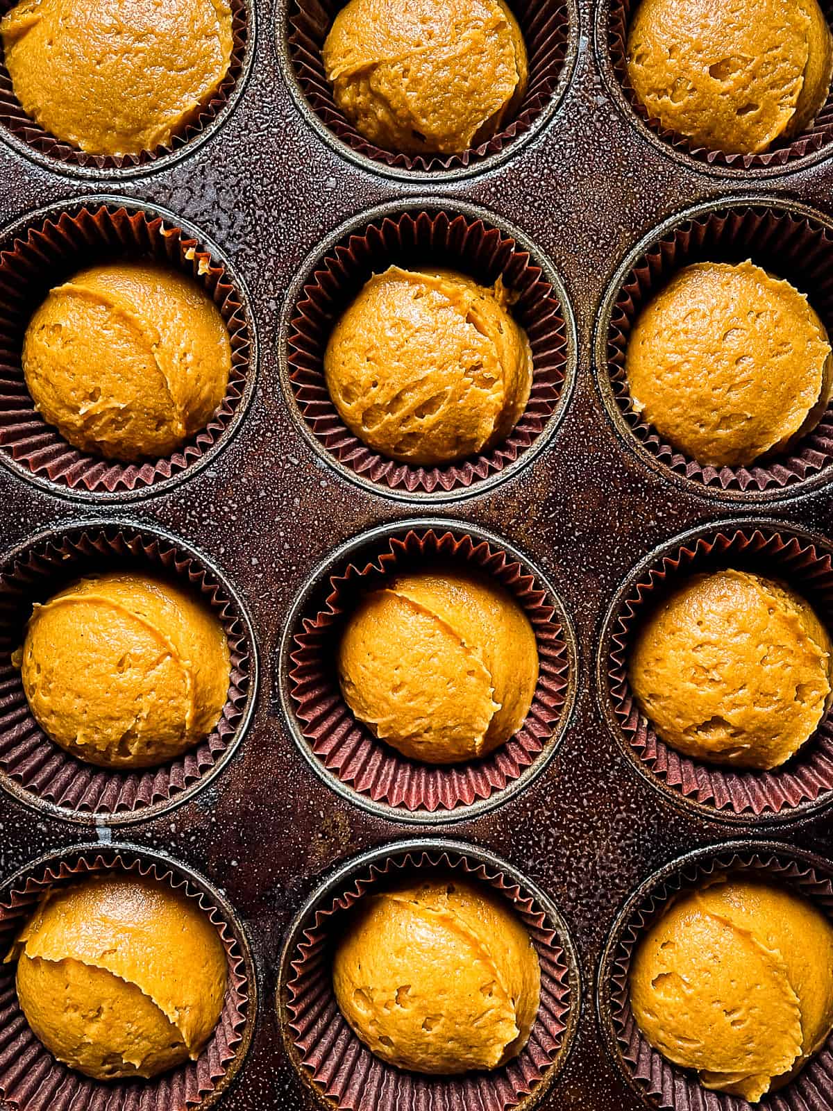 Pumpkin muffin batter in the paper-lined and greased pan.