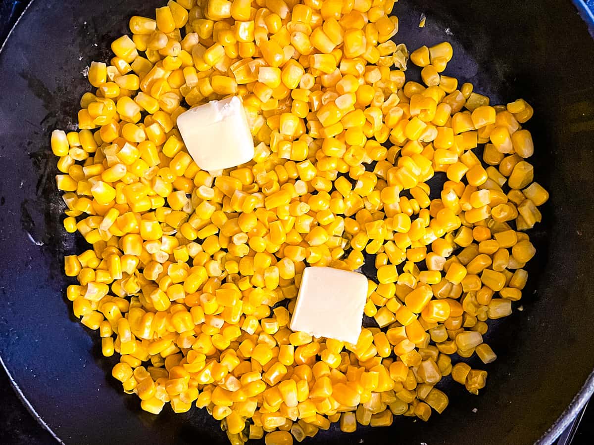 Frozen corn in a skillet with two pats of butter.