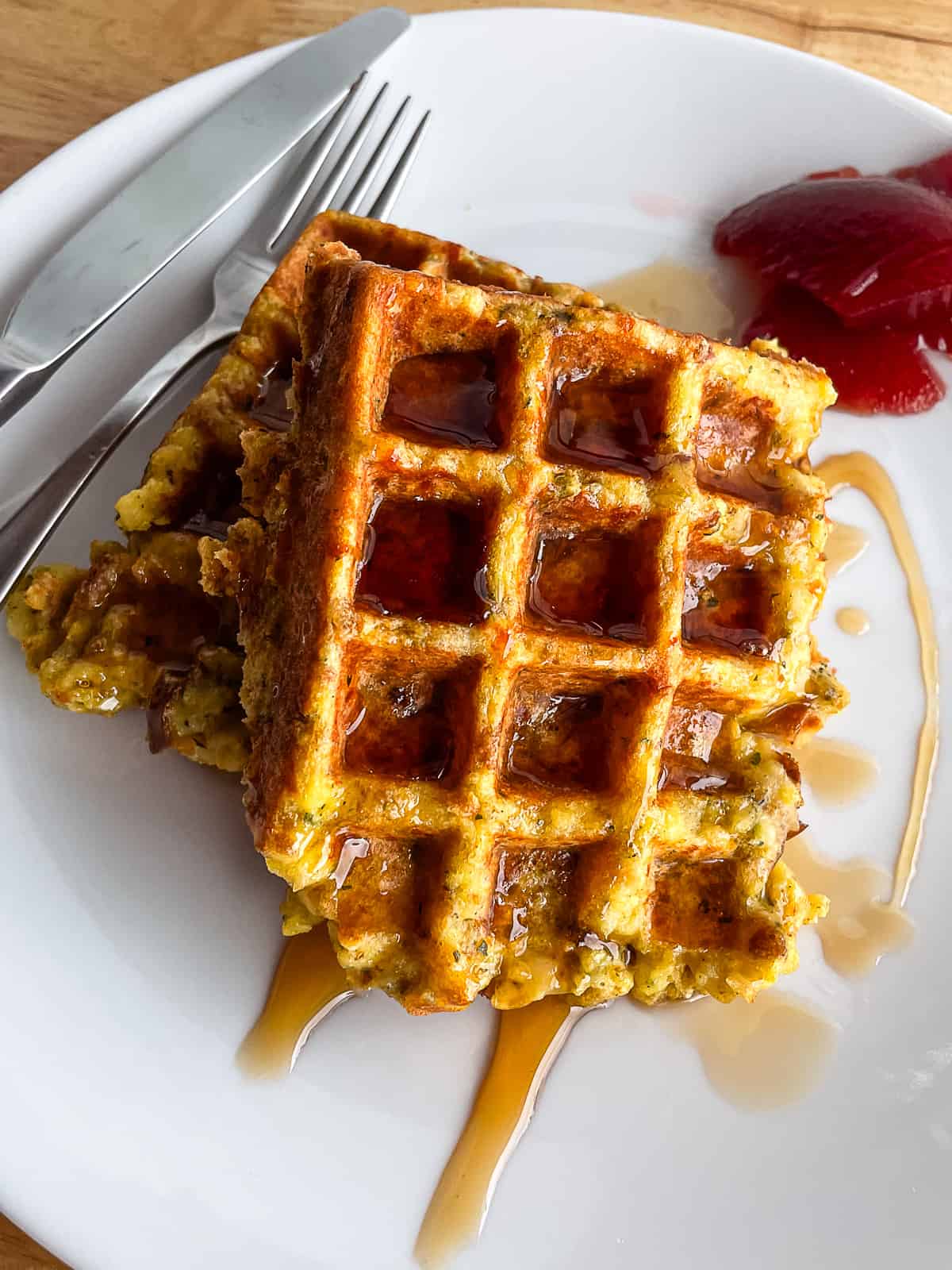 Stuffing waffles drizzled with maple syrup and leftover cranberry sauce on a plate.