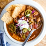 A bowl of chicken tortilla soup topped with sour cream, minced red onions, pickled jalapeños, and tortilla chips.