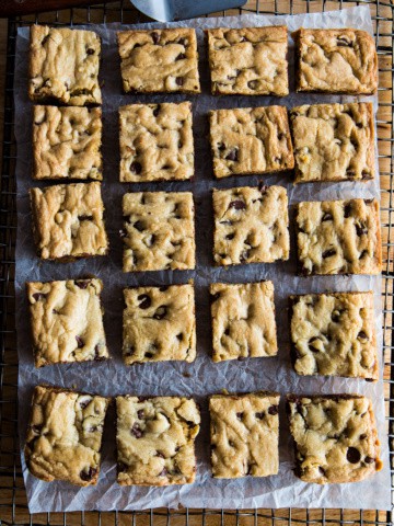 Chocolate chip cookie bars on cooling rack with parchment underneath.