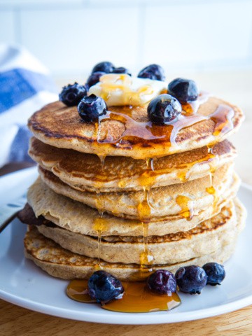 A stack of oat flour pancakes with maple syrup, blueberries, and butter.