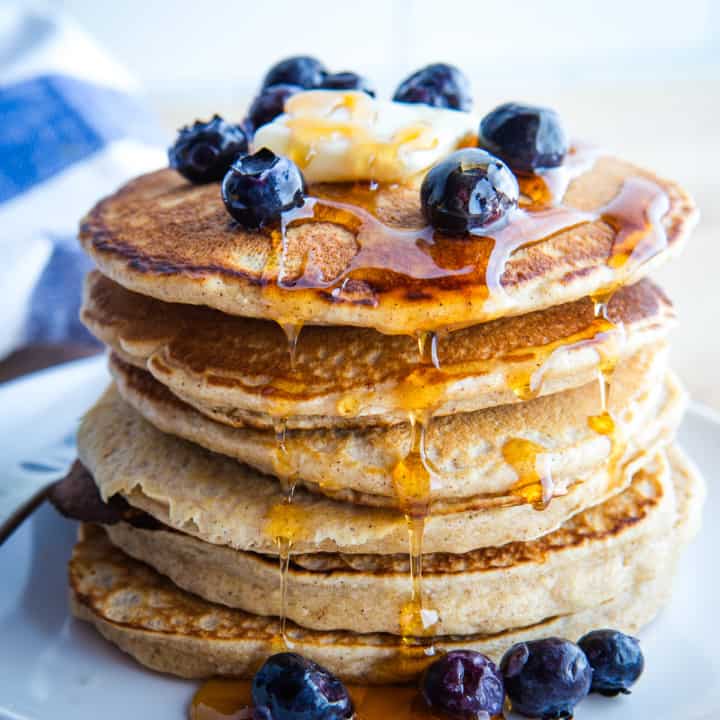 A stack of oat flour pancakes with maple syrup, blueberries, and butter.