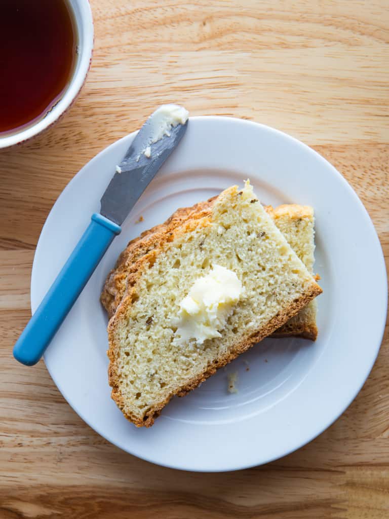 Two slices of caraway soda bread with a pat of butter on a small plate.