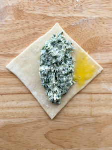 Filled spinach puff pastry with the right corner brushed with whisked egg.
