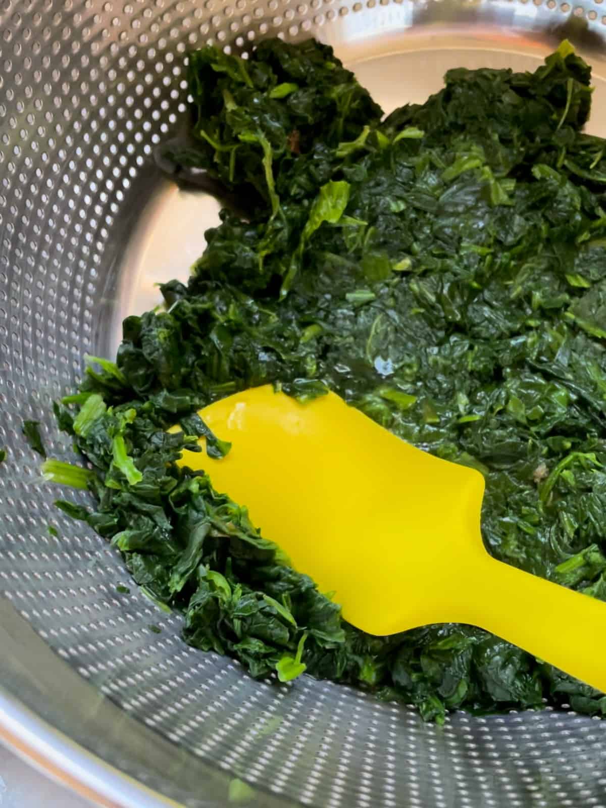 Pressing liquid out of thawed spinach. This is being done in a colander with a silicone spatula. 