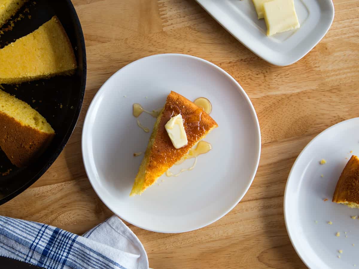 Slice of cornbread on a plate with a pat of butter and drizzle of honey.