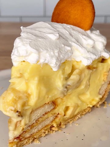 Slice of banana pudding pie topped with whipped cream and a vanilla wafer.