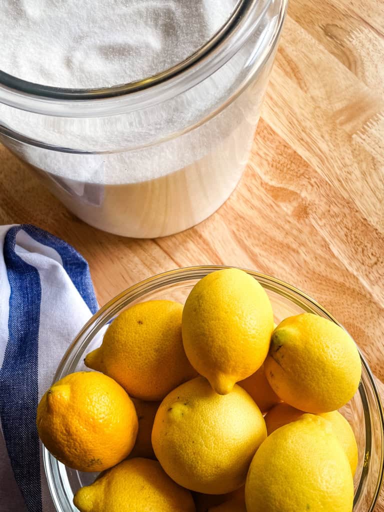 A canister of granulated sugar and a bowl of fresh lemons. These are two of the ingredients for homemade lemonade.