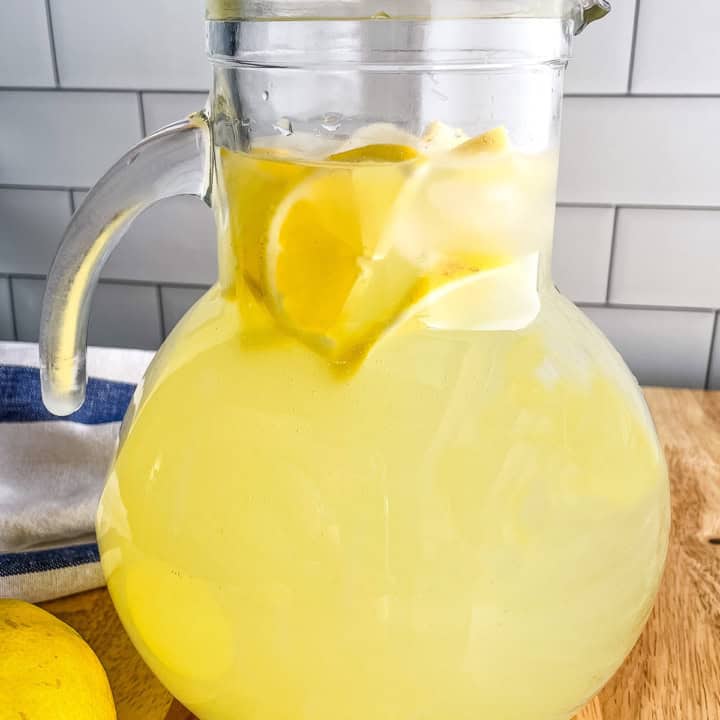A pitcher of homemade lemonade with lemon slices and ice cubes floating on top.
