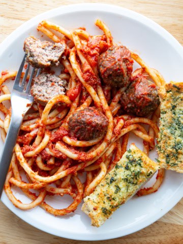 Air fryer meatballs on a plate with spaghetti and garlic bread.