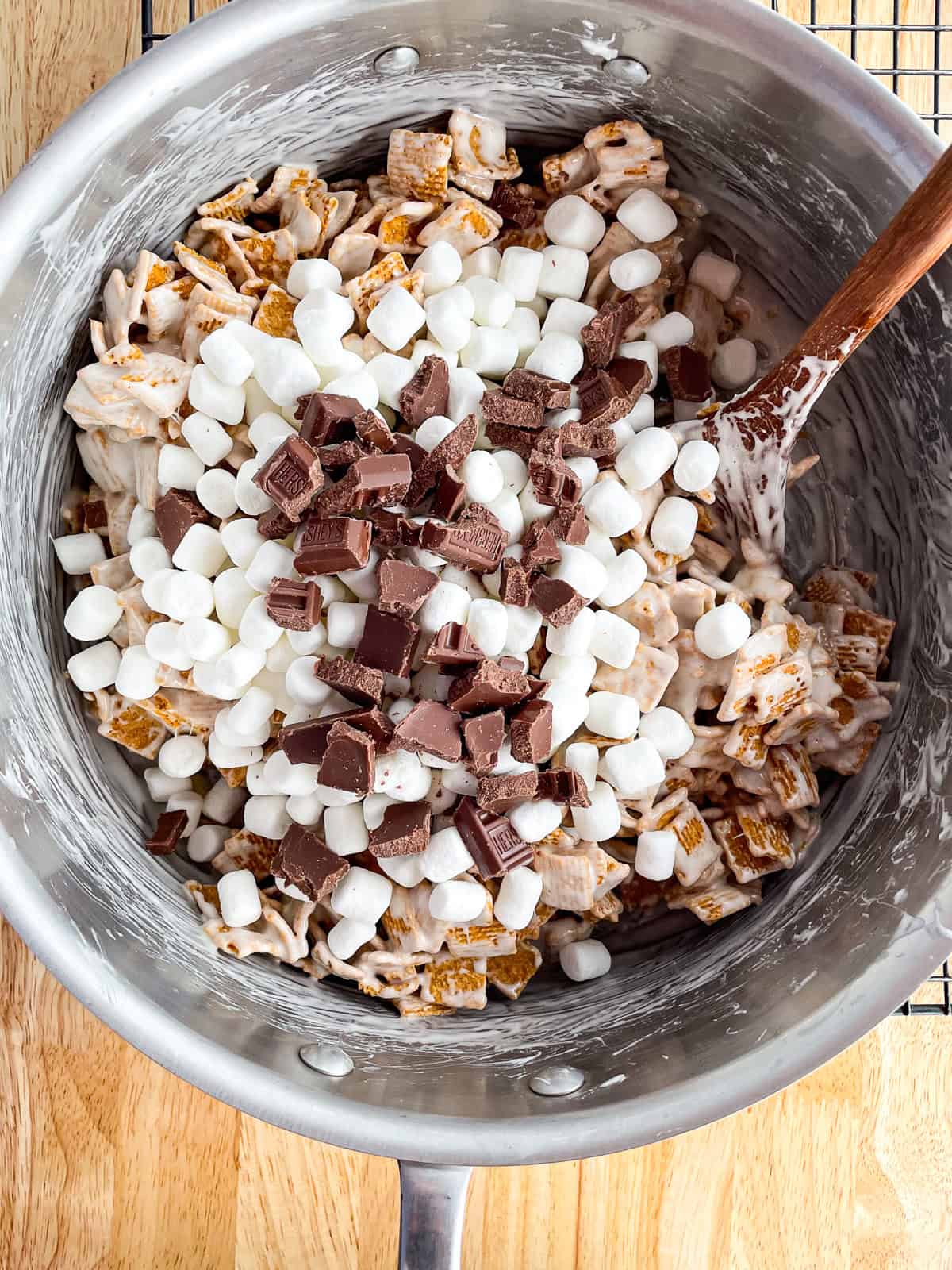Adding mini marshmallows and chopped chocolate to the cereal mixture.